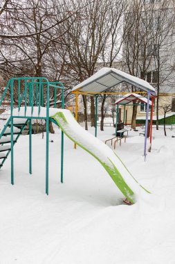 Karla kaplı kaydırak seti, soğuk mevsimde sakin bir sessizlik ve duraklayan çocukluk oyununu gösteren bir kış oyun parkında boş duruyor..