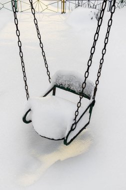 Terk edilmiş çocuk parkı salıncağı derin karlarla çevrili, sakin kış havasını, soğuk iklimi ve durgun çocukluk aktivitelerini yakalıyor..