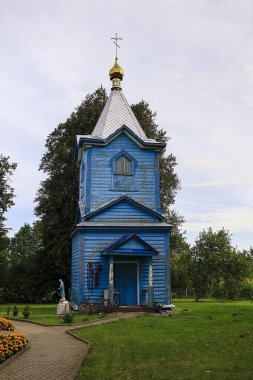 Geleneksel mavi ahşap Ortodoks kilisesi yeşil ağaçların arasına kurulmuş, ruhani mirası, kırsal yerleşimi ve klasik ahşap işçiliği sergiliyor..
