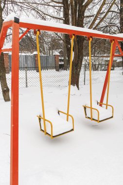 Taze kara gömülü parlak kırmızı ve sarı salıncaklar, kışın şehir merkezinde terk edilmiş oyun alanlarını gösteriyor..
