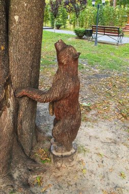 Oyun parkının yakınındaki bir ağaca bağlanmış el oyması ahşap ayı yeşil bir parktaki kırsal alanda ustalıkla yaratılmış eğlenceli bir doğa yaratıyor..