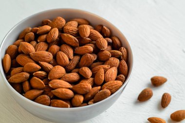 Beyaz arka planda, minimalizm, dengeli beslenme ve bilinçli yaşam tarzı değerlerini doğal ve sağlıklı gıdalarla ifade eden bademlerle dolu bir kase. Boşluğu kopyala.