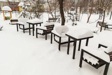 Soğuk iklimi, durgunluğu ve günlük şehir ortamını vurgulayan, oyun parkının yakınındaki derin karla kaplı bankların olduğu şehir parkı sahnesi.