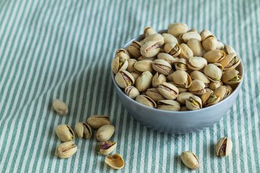 Çizgili kumaş arka planda bir kase kavrulmuş şam fıstığı. Doğal ışık ve basit kompozisyon içeren sağlıklı bir atıştırma konsepti sergiliyor. Boşluğu kopyala.