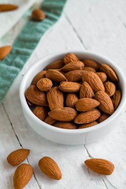 Beyaz bir kasede beyaz tahta bir masanın arka planında az miktarda badem sahnesi..