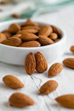 Tahta bir masanın üzerinde duran seramik bir kasedeki sağlıklı bademler, temiz ve doğal bileşimler..