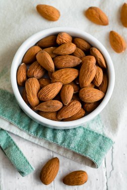 Beyaz bir seramik kasedeki bademler, beyaz bir peçetenin üzerine yerleştirilmiş, basit ve doğal besinler, hala hayattadır..