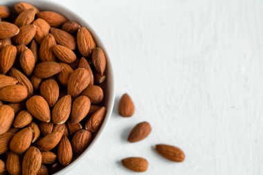 Beyaz arka planda saflık, doğal malzemeler, sağlıklı atıştırmalıklar ve minimalist bir görsel tarzda kasten yenen bademlerle dolu bir kase. Boşluğu kopyala.