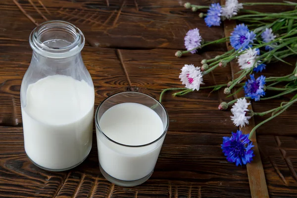 Fles met melk en glas melk aan houten tafel. — Stockfoto