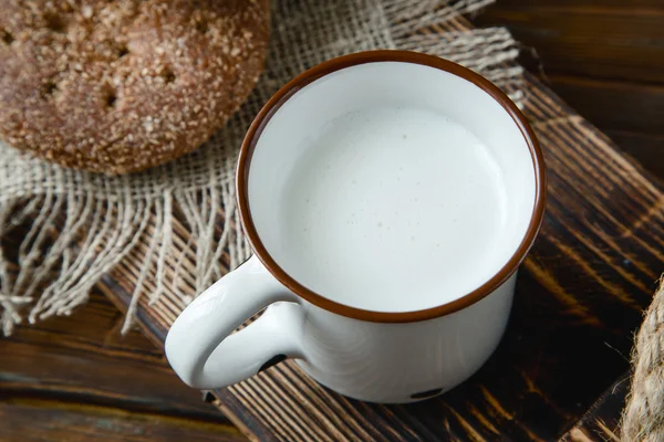 Tasse de lait chaud et pain sur fond de bois — Photo