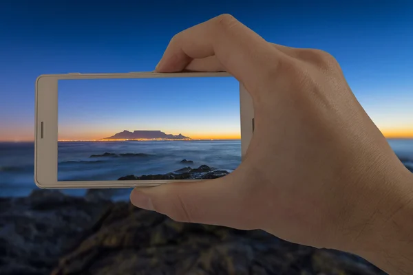 Tourist taking mobile photo of Cape Town Table Mountain at sunset.