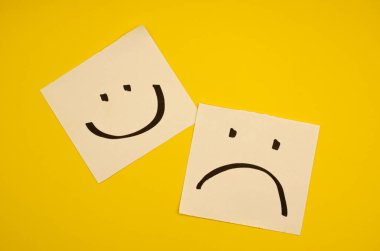 Sarı arka planda mutlu ve üzgün yüzler zihinsel sağlık farkındalığı ve çeşitli duygular konsepti için zıt duygu ve ruh hallerini ifade eder.