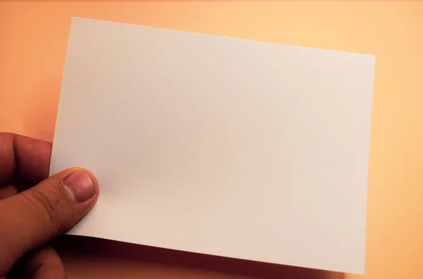 Sıcak şeftali arkaplanına karşı mesaj oluşturulması için elinde boş bir beyaz kart, duyurular, davetiyeler veya notlar için mükemmel.