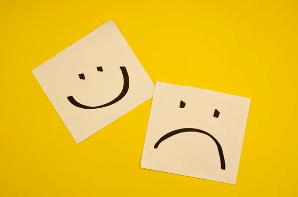Sarı arka planda mutlu ve üzgün yüzler zihinsel sağlık farkındalığı ve çeşitli duygular konsepti için zıt duygu ve ruh hallerini ifade eder.