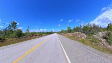 6. Otoyol 'da sahne sürüşü. Rocky Doğa Dağı manzarası ileri sürüş plakası. Yazın Yeşil Orman ve Kanada Kalkanı. Manitoulin Adası, Ontario, Kanada 'da asfalt yolda POV kullanıyor..