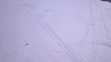 Kar araçlarının hava aracı görüntüleri, parlak güneşli güneş ışığı altında taze kış karının üzerindeki kavisli rayların desenlerini belirler. Donmuş Simcoe Gölü, Cooks Körfezi, Innisfil, Kanada 'da buzda balık tutma sporu.