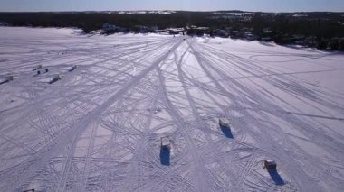 Kar araçları, atv ve buzda balık avlama kızakları ya da güneşli bir kış gününde taze kar yüzeyini gösteren kızak izleri karmaşık çizgiler ve gölge dokusu desenleri yaratıyor. Donmuş göl karlı manzara.