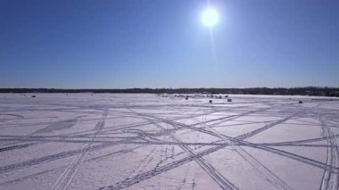 Kar araçları, atv ve buzda balık avlama kızakları ya da güneşli bir kış gününde taze kar yüzeyini gösteren kızak izleri karmaşık çizgiler ve gölge dokusu desenleri yaratıyor. Donmuş göl karlı manzara.