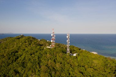Telekomünikasyon kulesi, iletişim anteni. Metal bir kulede tekrarlayıcılar. Tepeler ve yağmur ormanlarıyla kaplı manzara, yukarıdan manzara. Tekrarlayıcıları olan kule.