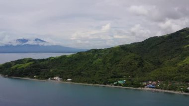 Mountains with forest at sea, against sky with clouds, top view. Luzon, Philippines. Mountain landscape on tropical island with mountain peaks covered with forest. Slopes of mountains with evergreen vegetation.