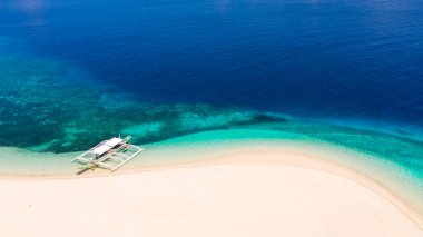 Beyaz kumdan oluşan tropik plaj, üst manzara. Sahilde bir turist teknesi. Turkuaz lagünlü mavi deniz. Yaz ve seyahat tatili konsepti. Sakin plaj sahnesi.