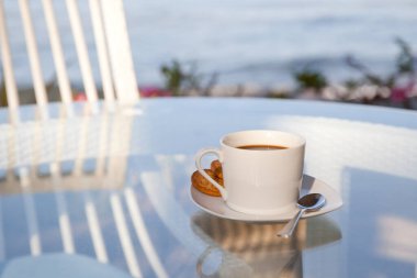 Şeffaf bir masada bir fincan kahve. Açık hava restoranındaki cam masa. Güneşli sabah