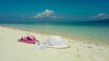 Kumsalda şapka ve sandaletler. Beyaz kumlu sahil ve mavi deniz.