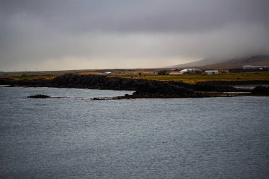 İzlanda kıyı köyü bulutlu gökyüzünün altında sisli tepeler ve sakin denizlerle