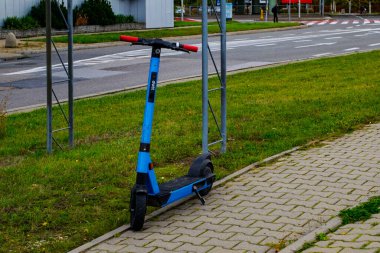 19 Ekim 2025, Varşova, Polonya: Büyük bir şehir yolu ve geçiş noktası yakınlarındaki kaldırım ve metal bariyere dayanan kaldırıma park etmiş mavi ortak elektrikli scooter (Dott markası).