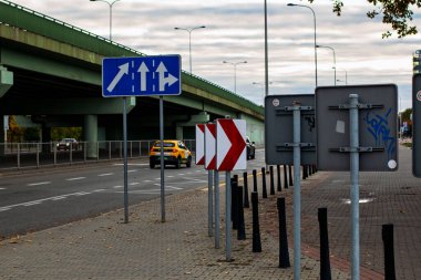19 Ekim 2025 'te, Varşova, Polonya' da birçok trafik ve yön işareti, bunların arasında üst geçit ve işlek şehir yolunun yakınındaki şerit kılavuz ve işaret levhaları ve sarı bir arabanın geçişi vardı.