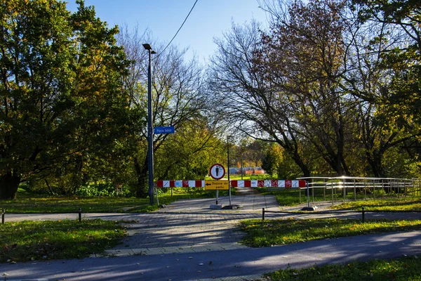 Polonya, Varşova, 2025. Kapalı park girişi, yaya levhası ve sonbahar ağaçları.