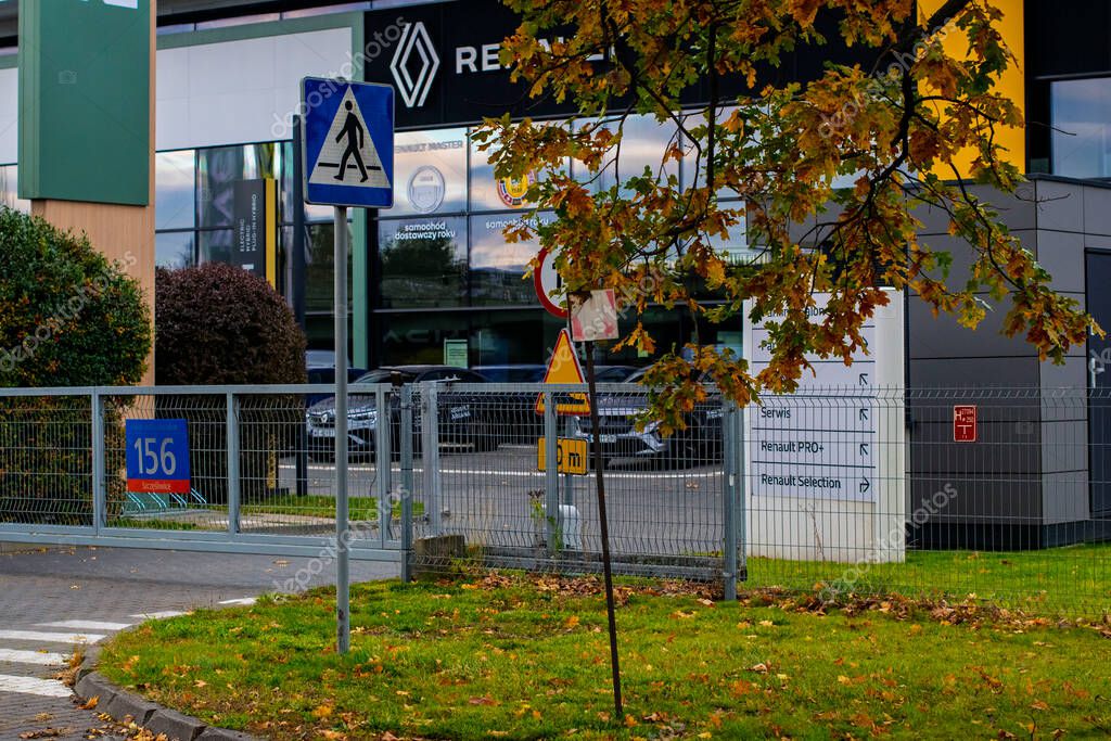 October 19, 2025, Warsaw, Poland: The exterior and fenced entrance of a Renault car dealership, featuring Polish traffic signs, service directories, and autumn tree foliage