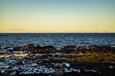 Kayalık kış kışı boyunca altın güneş ışığı ve koyu mavi deniz.