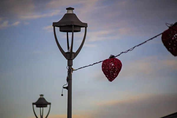 Günbatımında kırmızı dekoratif kalp ışıkları olan sokak lambası.