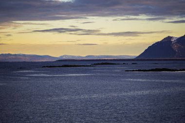 Gün batımında dağlarla ve kayalık adalarla sakin okyanus manzarası