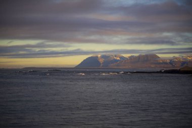 Gün batımında Sakin Kıyı Sularının Üzerinde Karlı Dağ Sırası