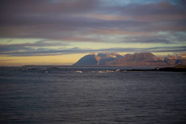 Gün batımında Sakin Kıyı Sularının Üzerinde Karlı Dağ Sırası