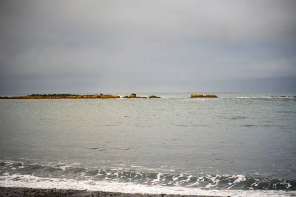 Bulutlu gökyüzünün altında kayalık resifli sakin okyanus dalgaları