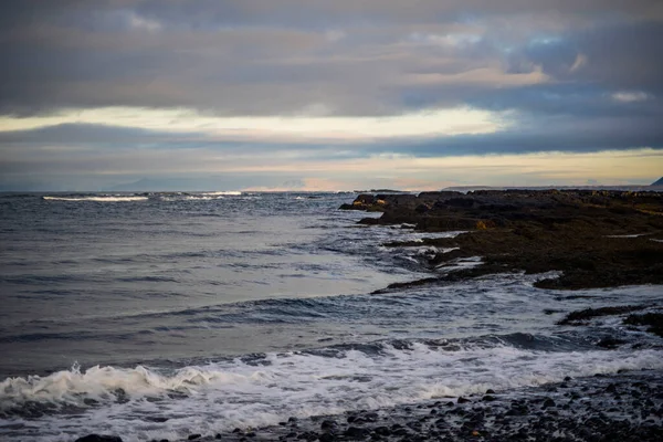 Dalgalar ve bulutlu akşam gökyüzü ile Rocky sahili