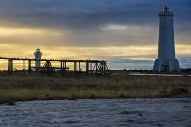 Sunset 'te iki deniz feneri ve kıyı manzaralı ahşap yapılar.