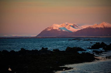 Snowy Mountain Range at Sunset Over Rocky Coastline