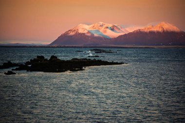 Snowy Mountain Range Above Dark Ocean at Sunset