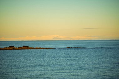 Gün batımında Uzak Karlı Dağlarla Sakin Deniz