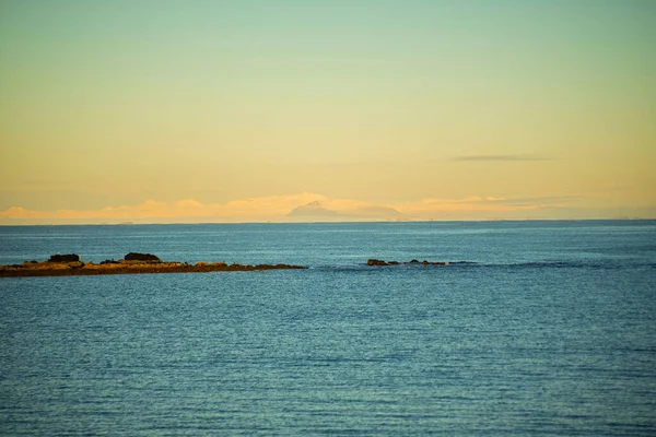 Gün batımında Uzak Karlı Dağlarla Sakin Deniz