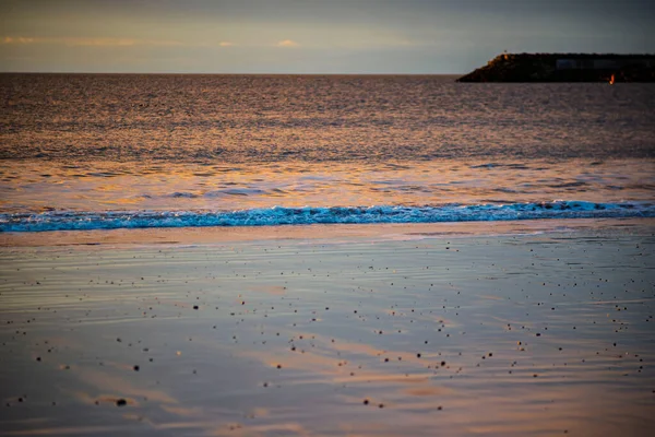 Sakin okyanus dalgaları ve kumlu sahilde gün batımı yansıması