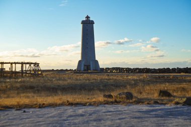 Akranes deniz feneri İzlanda 'da çimenli bir sahilde gün batımında mavi gökyüzünün altında duruyor.