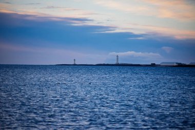 Sakin bir okyanusun ötesindeki uzak bir adada deniz fenerleri yumuşak bir akşam gökyüzü altında, Akranes, İzlanda