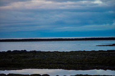 Sakin Mavi Deniz ve Yansıtıcı Gelgit Havuzları ile İzlanda Sahili üzerinde Huysuz Alacakaranlık