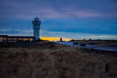 Alacakaranlık 'taki Beyaz Kıyı Deniz fenerinin canlı turuncu Horizon ve Moody Blue Sky ile sinematik görüntüsü