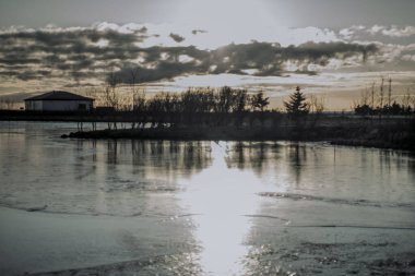 İzlanda 'da Kabin ve Ağaç Yansımalarıyla Donmuş Göl Üzerinde Dramatik Kış Günbatımı